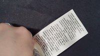 Main tenant une étiquette d'entretien de vêtement avec la composition du tissu et les instructions de lavage en plusieurs langues sur un fond sombre.