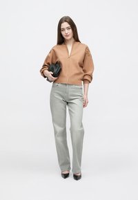 Brun bomberjakke med lynlåslukning foran, ribbet kant og broderede detaljer, kombineret med lysgrå jeans og sorte højhælede sko.