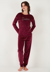 Burgundski velur pajama set z dolgimi rokavi, ki vsebuje napis "sledi svojim sanjam" ter ujemajoče se hlače z elastičnim pasom.