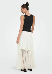 Zwarte mouwloze top gecombineerd met een gelaagde, doorschijnende witte maxirok. Zwarte flats met zilveren studs maken de look compleet.