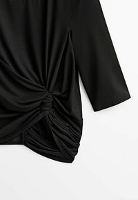 Haut noir à manches longues avec un détail de nœud torsadé et un tissu froncé sur un côté, présenté sur fond blanc.