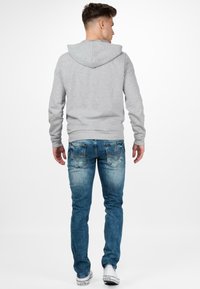 Sweatshirt gris à capuche avec de longues manches, associé à un jean en denim bleu avec un délavage subtil et des poches arrière cousues, porté avec des baskets blanches.