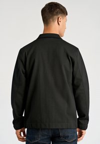 Czarna kurtka o prostym kroju, z długimi rękawami i kołnierzem. Wykonana z teksturowanej tkaniny, z widocznymi detalami przeszyć. Luźny krój.