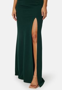 Abito maxi verde aderente con uno spacco alto fino alla coscia, realizzato in un materiale liscio e elastico. Presenta un design a silhouette elegante senza motivi visibili.