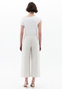 Bílý top s krátkým rukávem v kombinaci s krémovými kalhotami s vysokým pasem a širokými nohavicemi. Hladká látka se strukturovaným střihem a minimalistickým designem.