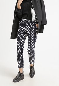 Pantaloni a scacchi bianchi e neri con una vestibilità slim, caratterizzati da un lunghezza cropped e tasche laterali, abbinati a sneaker alte nere.