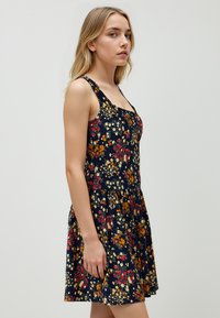 Abito floreale con sfondo navy e fiori rossi, gialli e bianchi. Forma ad A, senza maniche, con scollo a giro.
