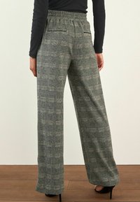 Hose mit weitem Bein in einem schwarz-weißen Karomuster, mit elastischem Bund und zwei Gesäßtaschen. Geschmeidige Stoffoberfläche.