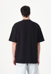 Tricou negru supradimensionat cu mâneci scurte, textură ribotată, guler tip crew și un design simplu, asortat cu blugi deschiși la culoare.