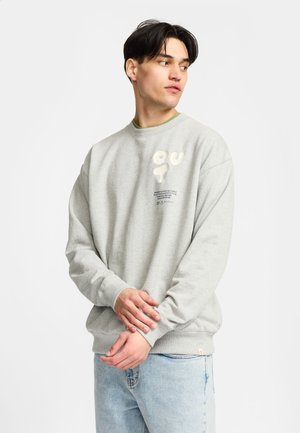 Grijze sweatshirt gemaakt van een katoenmix, met ribbels aan de manchetten en onderkant, met "OUT" in het wit geborduurd. Draag over een groene shirt.