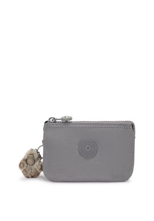 Cartera de nylon gris con una textura suave, cierre con cremallera y un logo circular. Presenta un charm peludo adjunto a la cremallera.