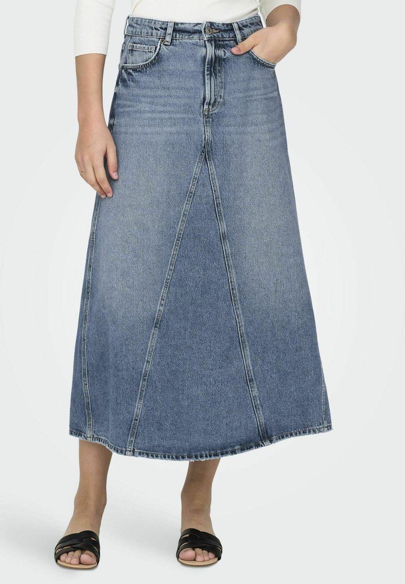 Jeansmaxikjol med hög midja, med vertikala sömmar, i en ljusblå tvätt och rå fåll. Bärs med svarta slidesandaler.