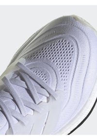 Witte sportschoen met een textuur van mesh bovenkant, dunne veters en plastic accenten. Heeft een ronde neus en een zwarte zool.