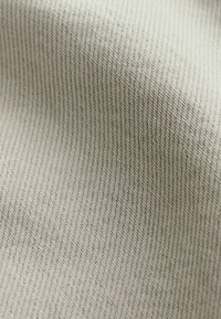 Gros plan sur un tissu beige avec une texture en armure sergée diagonale montrant des fils fins et réguliers ainsi que des plis doux.