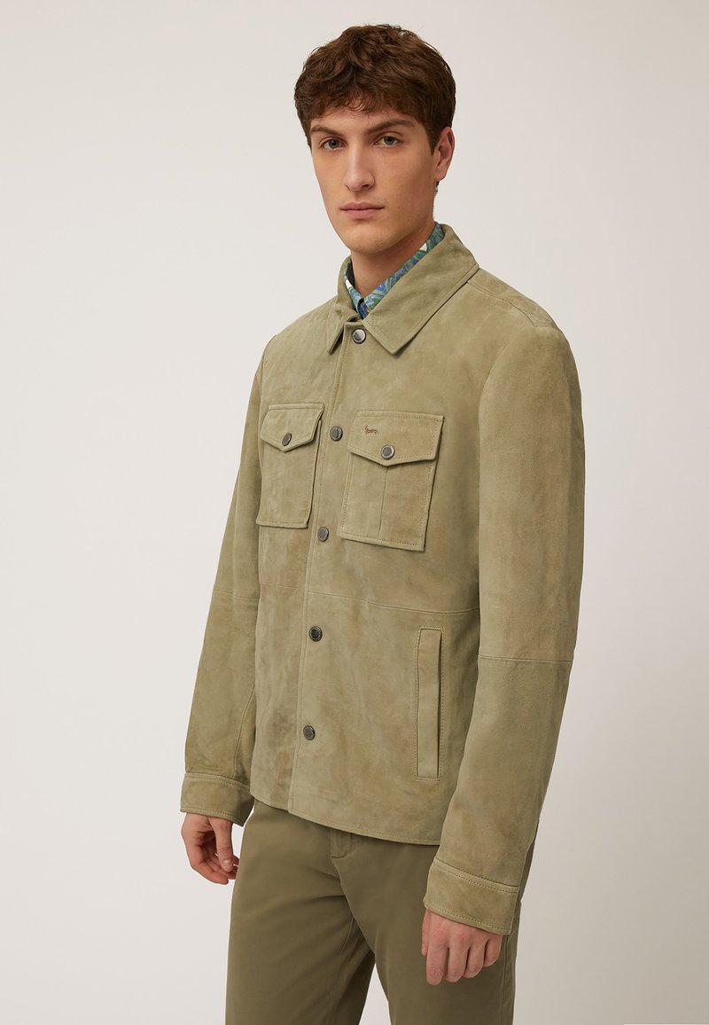 Veste en cuir suédé vert clair avec un devant à boutons, deux poches poitrine et un col pointu. Elle présente une texture lisse et des détails de couture subtils.