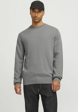 Suéter gris hecho de una tela suave con un cuello redondo y puños acanalados, combinado con jeans oscuros. Diseño simple y casual sin patrones.
