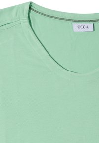 T-shirt en coton vert clair avec un col rond et une étiquette blanche marquée "CECIL" cousue à l’intérieur du col.