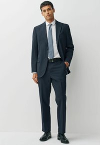 Navy suit with a classic fit; single-button jacket, flat-front trousers, white dress shirt, patterned tie, and black leather shoes.
