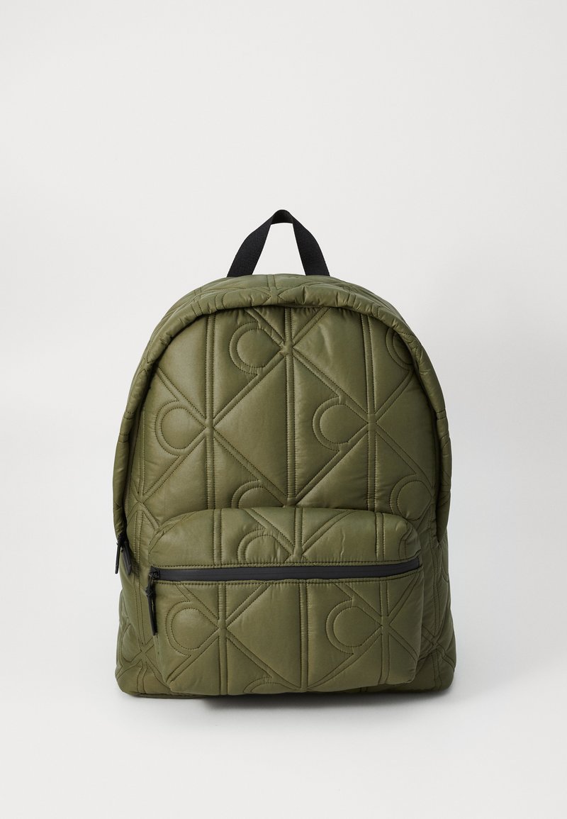 Sac à dos olive matelassé de forme arrondie, avec une fermeture éclair noire et des coutures d'accent en motif de losange. Il dispose d'une poignée supérieure et de bretelles.