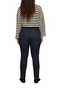 Dunkelblaue Skinny Jeans mit hoher Taille, die dezente Gesäßtaschen und eine glatte Textur aufweisen, kombiniert mit einem gestreiften, cropped Langarmoberteil.
