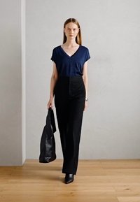Navy V-Ausschnitt T-Shirt mit kurzen Ärmeln, kombiniert mit hoch taillierten schwarzen Hosen. Eine schwarze Tasche und Schuhe runden das Outfit ab. Glatte Texturen.