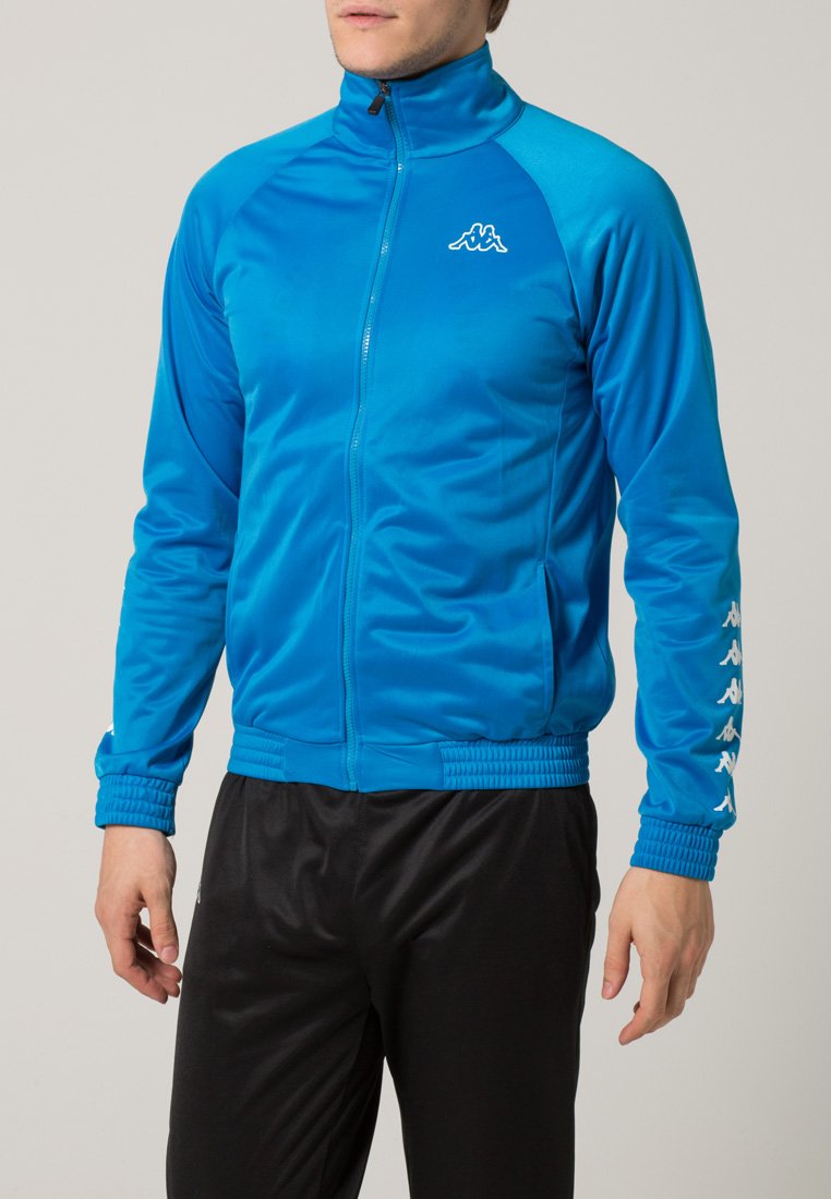 Giacca atletica blu con zip realizzata in un tessuto leggero e liscio. Presenta tasche laterali, polsini elasticizzati e il logo Kappa sul petto e sulle maniche.