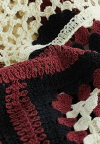 Kötött takaró texturált mintával bordó, fekete és krémszínben, ívelt szélekkel és kör alakú motívumokkal.