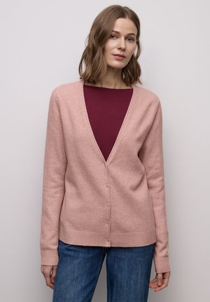 Cardigan rose clair en tissu doux, avec un col en V profond, des boutons à l'avant et des poignets côtelés, associé à un haut bordeaux et un jean bleu.