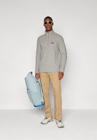 Sivi flis pulover s polovičnim zadrgo, rjave hlače in svetlo modra nahrbtnik. Sive superge s temnimi poudarki dopolnjujejo obleko.