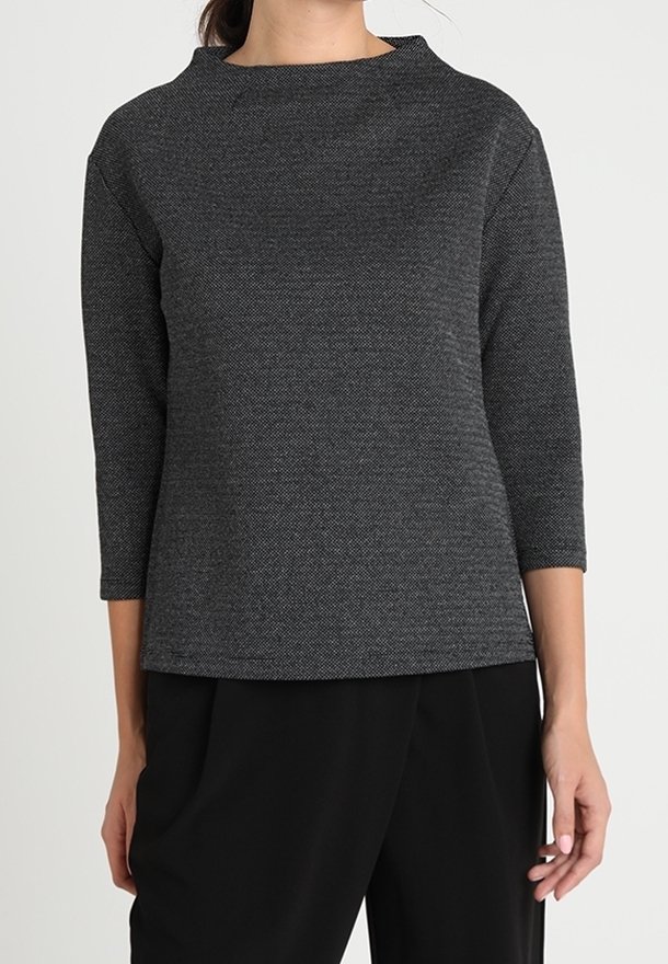 Top de manga larga en negro jaspeado con escote barco y corte holgado. Fabricado en un material texturizado, combinado con pantalones anchos negros.