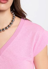 T-shirt rosa chiaro con scollo a V realizzata in tessuto morbido, caratterizzata da maniche corte e una trama sottile, abbinata a una collana con perline rotonde in argento lucido.