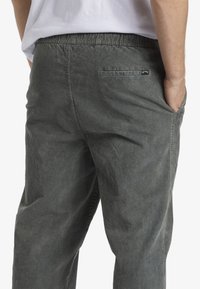 Pantalones de sarga grises con un corte relajado, que cuentan con una cintura elástica, bolsillos laterales y un bolsillo trasero con un pequeño parche de logo.