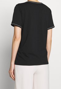 Schwarzes T-Shirt mit kurzen Ärmeln und rundem Halsausschnitt, mit weißer Einfassung an Ärmeln und Halsausschnitt. Weicher, glatter Stoff.