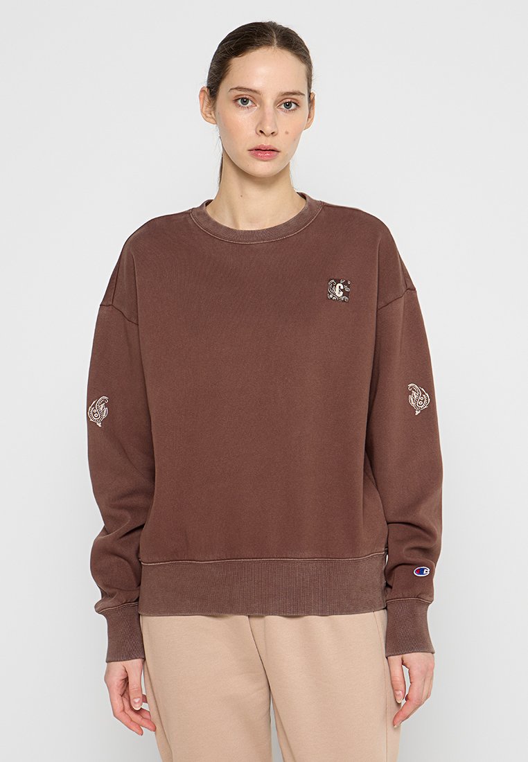 Brauner Baumwollpullover mit gerippten Bündchen und Saum, featuring ein kleines Logopatch auf der Brust und dekorativer Stickerei an den Ärmeln.