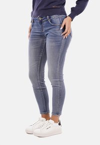Jeans skinny in denim azzurro chiaro con un lavaggio sbiadito, caratterizzati da cinque tasche, una zip frontale e una chiusura a bottone classica, abbinati a sneakers bianche.