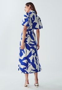 Mėlyna ir balta lininė suknelė su pūstomis rankovėmis, vidutinio ilgio, su lapų raštu ir savišvytu diržu ties liemeniu.