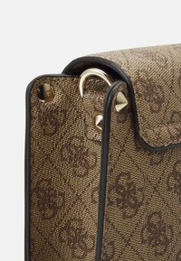 Brązowa torebka o fakturowanej powierzchni, z ozdobnym złotym metalowym kółkiem i czarną lamówką. Na zewnętrznej stronie delikatny wzór z logo.