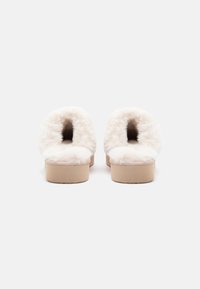 Hvide plyssandaler med åben hæl, blød pelsstruktur og en lys tan gummisål. Rund tådesign og minimal pynt.