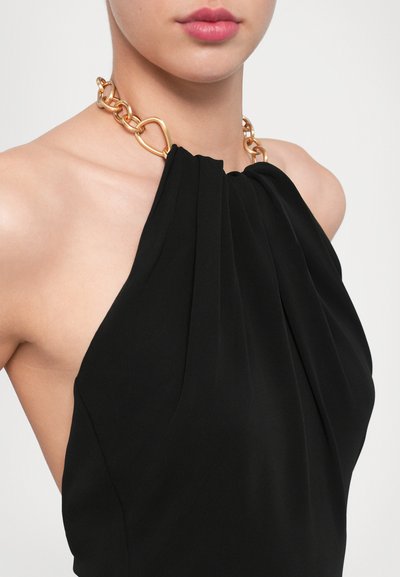 Sort halterneck kjole med plisseret stof og en guld kædetråd med hjerteformede led, der fremhæver den glatte tekstur og det elegante design.