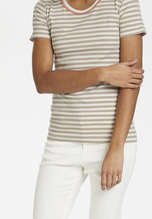 Pruhované béžovo-krémové žebrované tričko s kulatým výstřihem a oranžovým akcentem. Nošeno s bílými kalhotami, rukáv a ruka jsou viditelné.