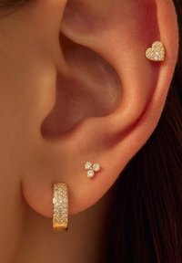Boucles d'oreilles en métal doré ornées de strass clairs, accompagnées d'un clou en forme de cœur et d'un groupe triangulaire de petites pierres sur l'oreille.