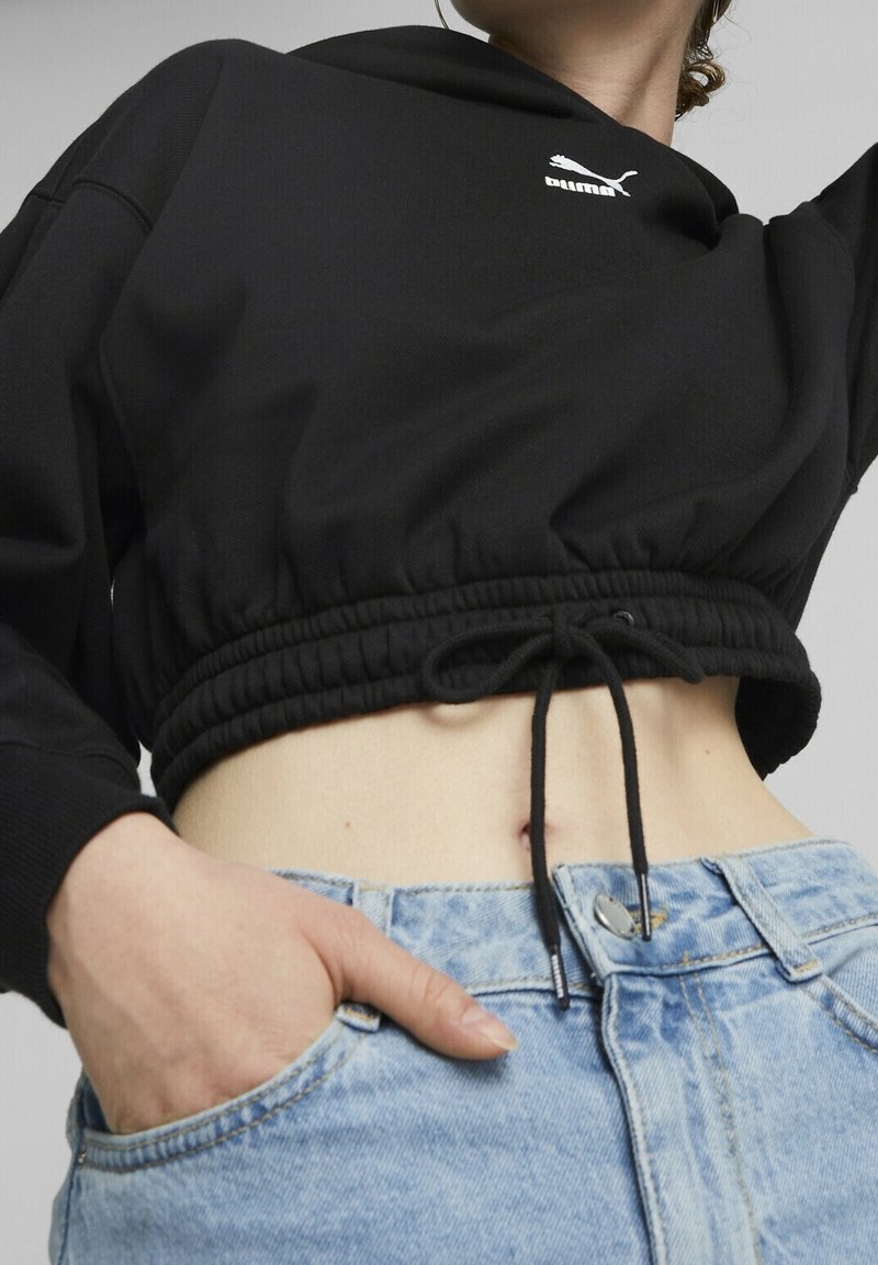 Felpa nera cropped con orlo a coulisse e logo sul petto, abbinata a jeans in denim blu chiaro con vita alta.