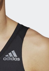 Débardeur de sport noir avec un col en forme de triangle, des coutures plates et un logo Adidas argenté sur la poitrine gauche.