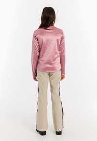 Roze satijnen langemouwen top met een kraag, gecombineerd met beige broek met zwarte zijkanten. Glad textuur, aansluitend ontwerp.