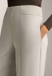 Svetlo sivi, krojeni hlače z rebrastim pasom, gladko teksturo, stranskimi žepi in subtilnimi detajli šivanja.