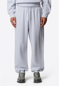 Ljusgrå sweatpants med elastisk midjeband och dragsko. Manschetter vid anklarna. Matchas med mörkgrå sneakers med gröna detaljer.