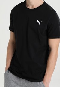 Svart bomullströja med korta ärmar, prydd med en liten vit Puma-logotyp på bröstet. Enkel, klassisk design med rund halsringning.