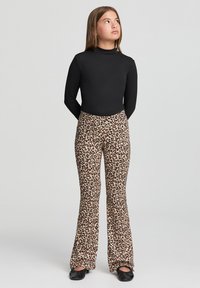 Maglietta nera a maniche lunghe abbinata a pantaloni a zampa d'elefante con stampa leopardata. I pantaloni presentano uno sfondo beige chiaro con macchie marrone scuro. Scarpe nere.