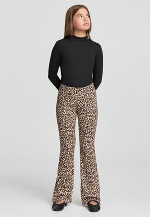 Maglietta nera a maniche lunghe abbinata a pantaloni a zampa d'elefante con stampa leopardata. I pantaloni presentano uno sfondo beige chiaro con macchie marrone scuro. Scarpe nere.