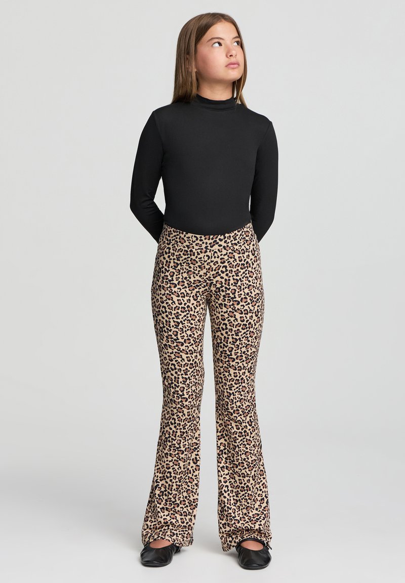 Maglietta nera a maniche lunghe abbinata a pantaloni a zampa d'elefante con stampa leopardata. I pantaloni presentano uno sfondo beige chiaro con macchie marrone scuro. Scarpe nere.